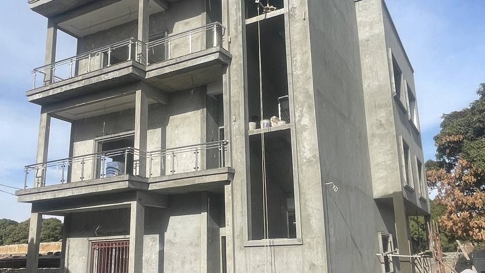 The Banjulinding structure at full height, its concrete frame and floor slabs cast and the walls rendered, with a balcony to each upper floor.