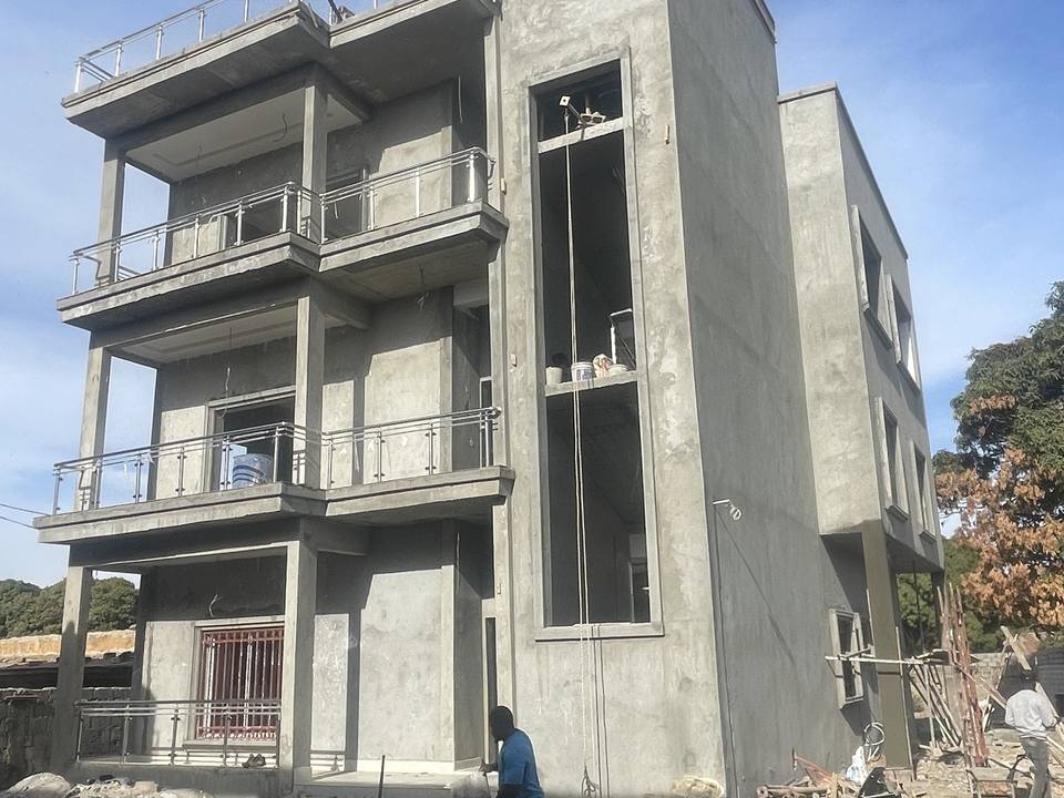The Banjulinding structure at full height, its concrete frame and floor slabs cast and the walls rendered, with a balcony to each upper floor.