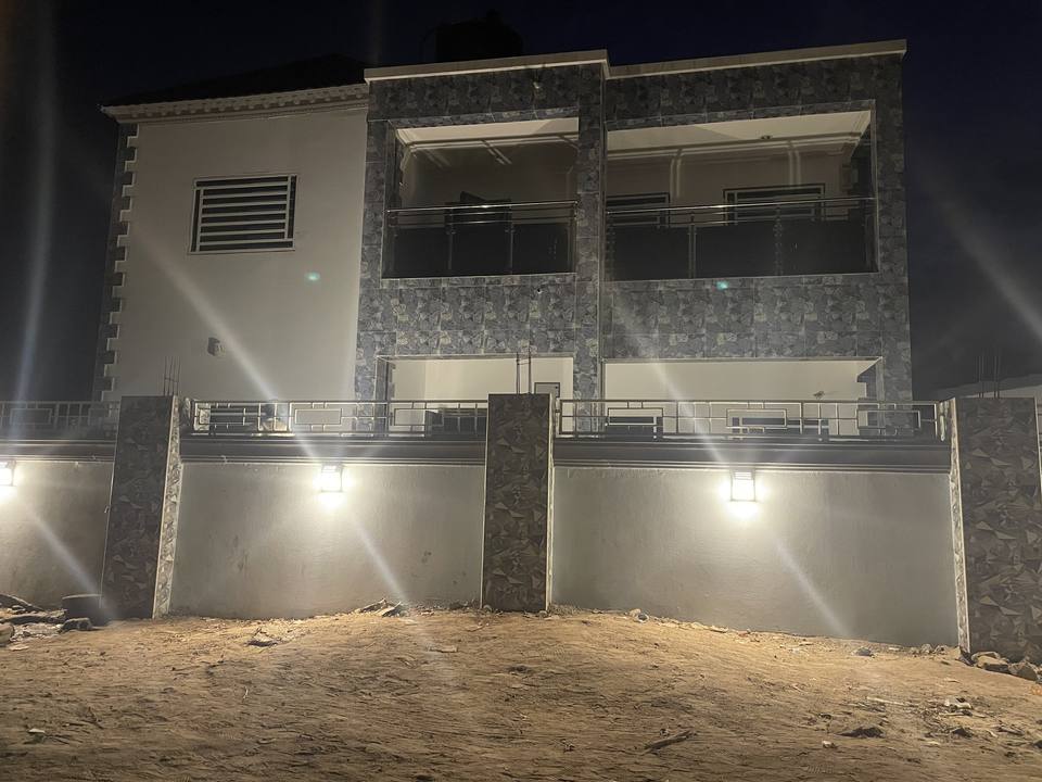 The front of the two-storey house at night, its stone-clad external walls lit from below.