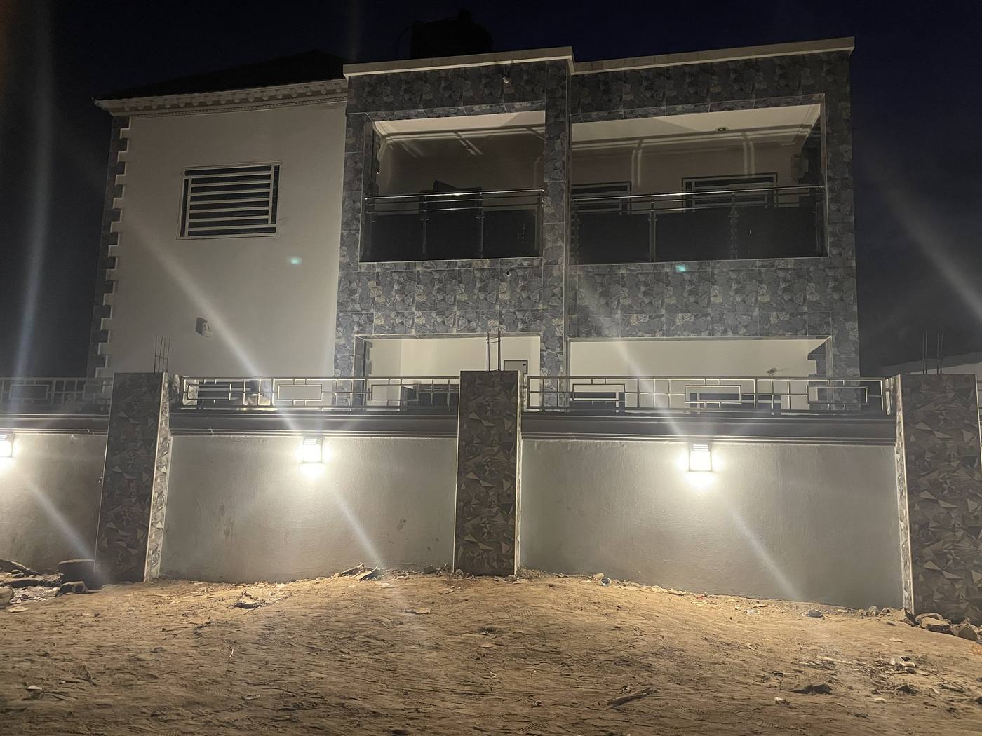 The front of the two-storey house at night, its stone-clad external walls lit from below.