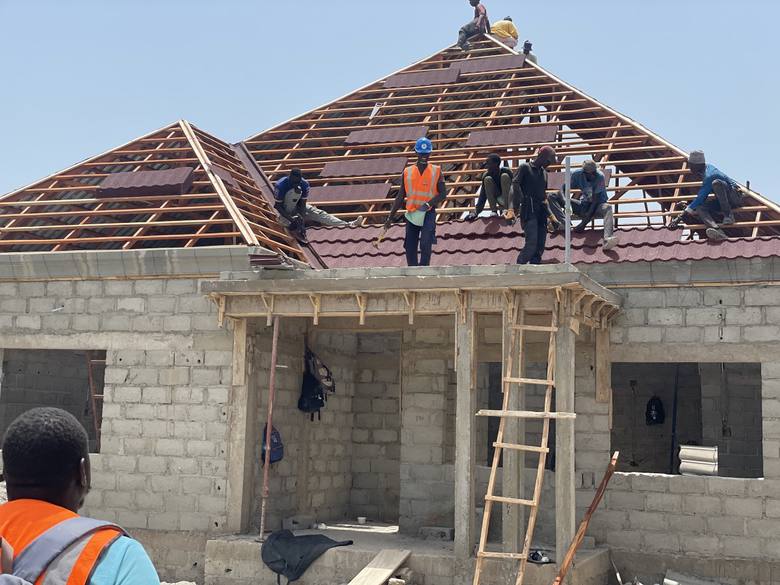 A crew laying roof tiles over the timber roof frame, the blockwork walls below still unrendered.