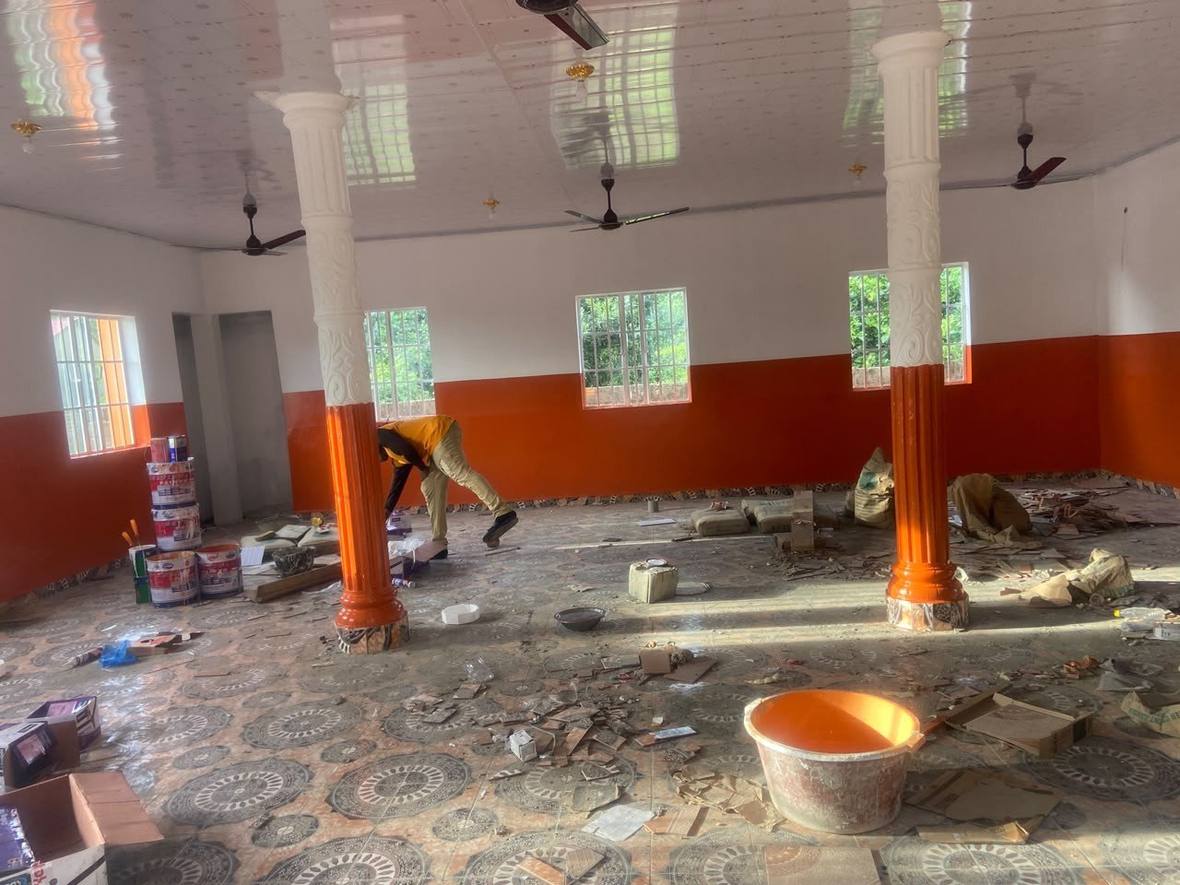A painter working along the dado of the prayer hall, the patterned floor tiles already laid and covered with offcuts.