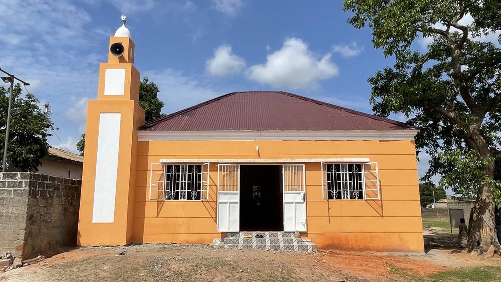 The completed exterior of Manduar Mosque, a single-storey prayer hall with a minaret rising at one corner.
