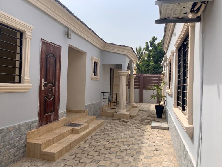 A paved passage between the wings of the house, with a side door and steps to the left and a gate at the far end.